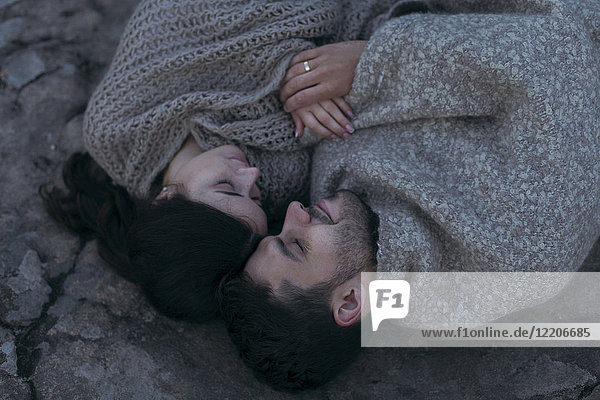 Kaukasisches Paar  das in eine Decke eingewickelt auf einem Felsen liegt