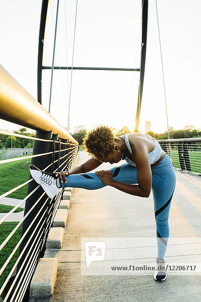 Mixed race woman stretching leg on bridge railing