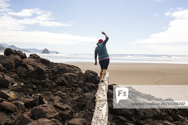 Caucasian woman balancing on log on rocks at beach