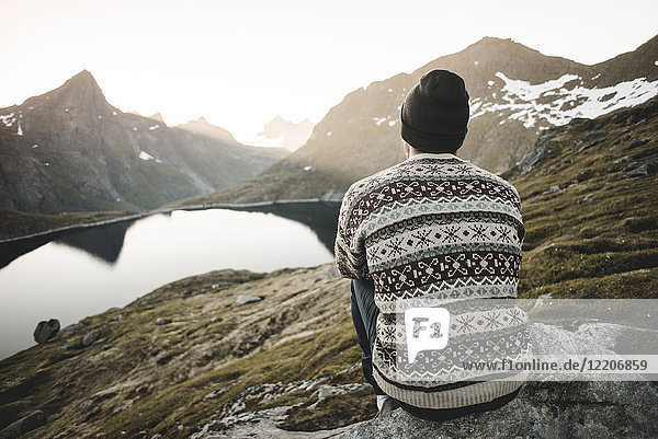 Kaukasischer Mann sitzt auf einem Felsen und bewundert die malerische Aussicht auf einen Bergsee