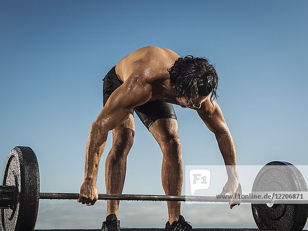 Sweating Hispanic man lifting barbell