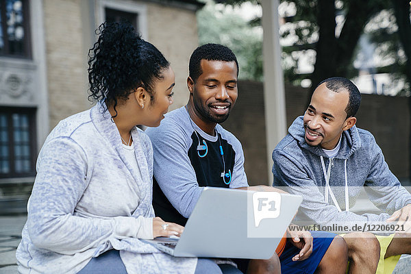 Black friends sitting outdoors using laptop