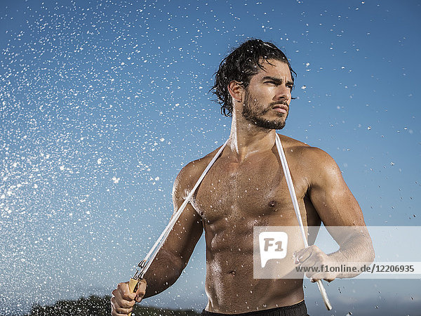 Water splashing on Hispanic man holding jump rope