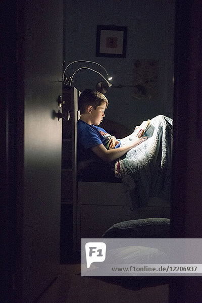 Caucasian boy reading book in bed at night