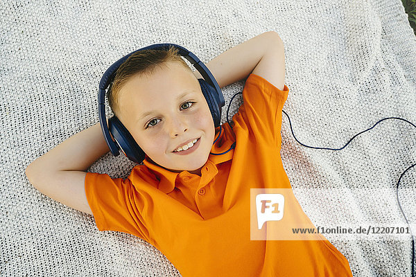 Smiling Caucasian boy laying on blanket in park listening to headphones
