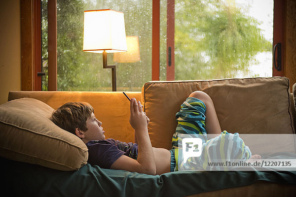 Caucasian boy laying on sofa texting on cell phone