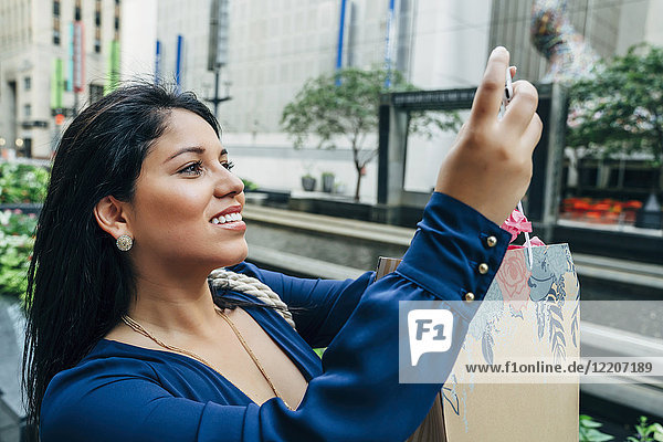 Hispanic woman with shopping bag posing for cell phone selfie