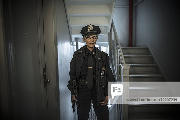 Portrait of older Caucasian policewoman holding gun in apartment staircase