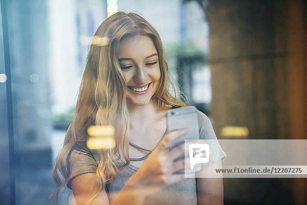 Smiling Caucasian woman posing for cell phone selfie behind window