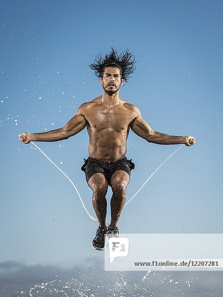 Water splashing on Hispanic man jumping rope