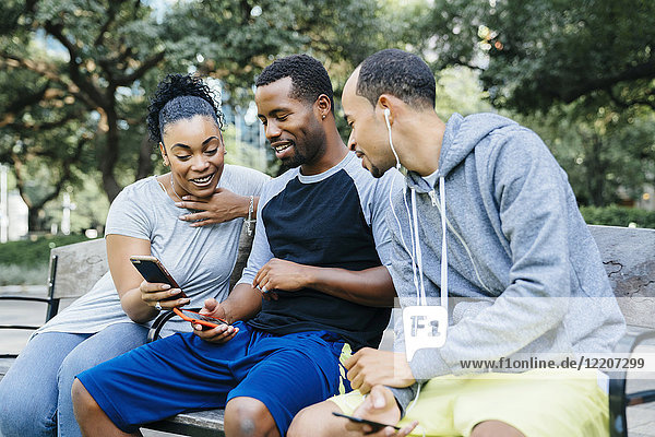 Black friends sitting on bench texting on cell phones