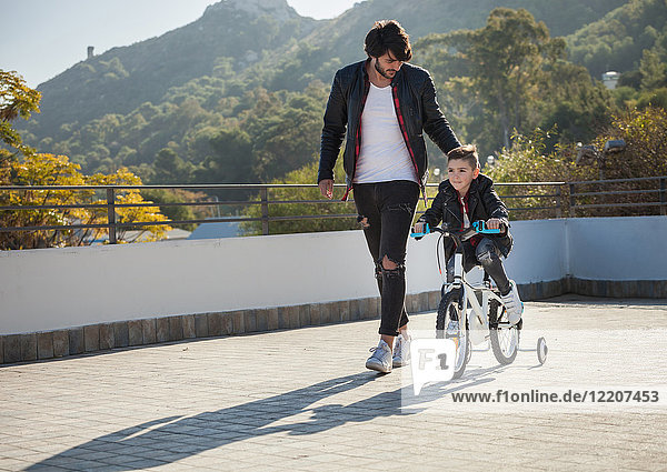 Junge Junge fährt Fahrrad mit Stabilisatoren  Vater geht neben ihm