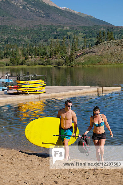Paddleboarding couple carrying paddleboard on lake shore  Frisco  Colorado  USA
