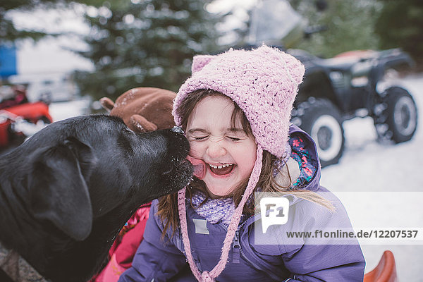 Junges Mädchen mit Hund in verschneiter Landschaft  Hund leckt Mädchen das Gesicht