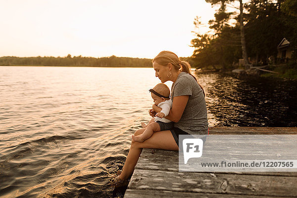 Mutter sitzt mit ihrer kleinen Tochter am Pier und schaut auf den See