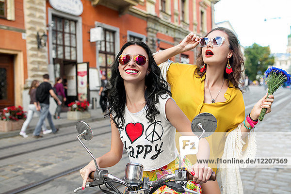 Porträt von zwei glücklichen Freundinnen mit Sonnenbrille auf dem Roller auf einer gepflasterten Straße  Odessa  Ukraine