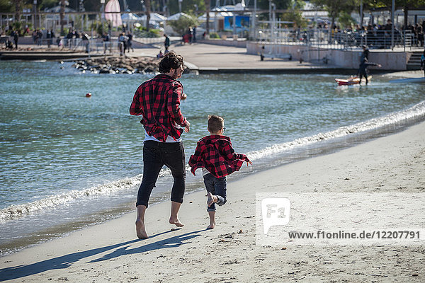 Vater und Sohn laufen am Strand entlang  Rückansicht