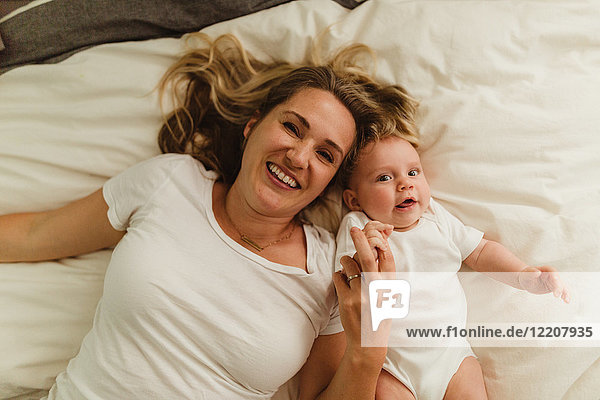 Overhead portrait of woman and baby daughter lying on bed holding hands