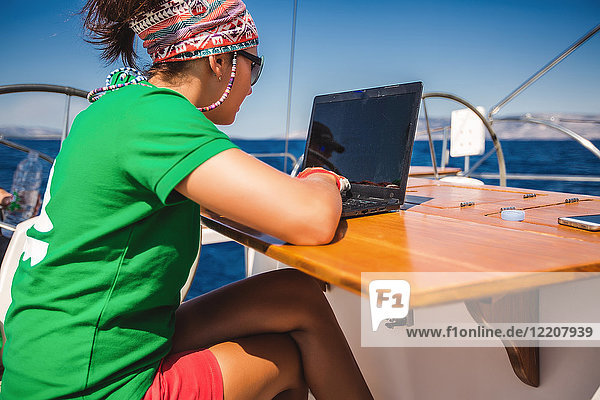 Junge Frau tippt am Laptop an Bord einer Yacht in Küstennähe  Kroatien