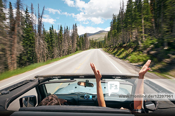 Road trip couple driving convertible on rural highway with hands raised  Breckenridge  Colorado  USA