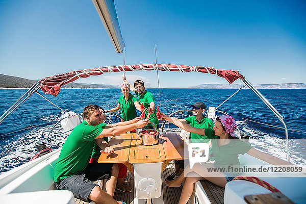 Männer und junge Frauen an Bord einer Yacht  die mit einer Wassermelonenscheibe anstoßen  Kroatien