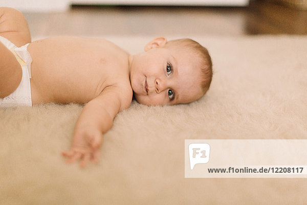 Portrait of cute baby girl in diaper lying on beige rug