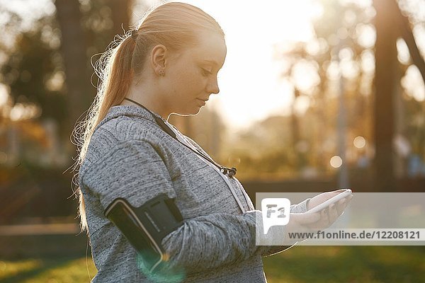 Kurvenreiche junge Frau trainiert im Park und sieht sich ein Smartphone an
