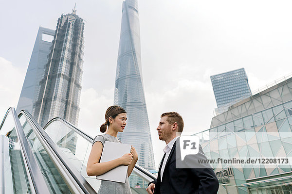 Junger Geschäftsmann und junge Geschäftsfrau bewegen sich auf der Rolltreppe im Finanzzentrum Shanghai  Shanghai  China