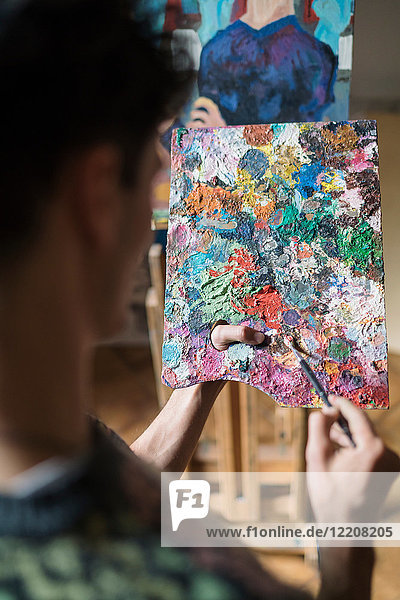 Über-Schulter-Ansicht eines männlichen Künstlers  der im Künstleratelier Ölfarbe auf einer Palette mischt