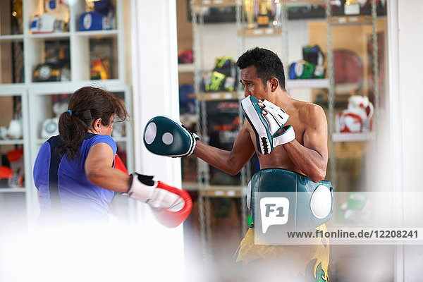 Mature woman practicing boxing with male trainer in gym