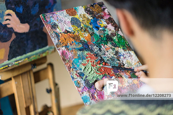 Männlicher Künstler beim Mischen von Ölfarbe auf Palette im Künstleratelier  Ansicht über die Schulter