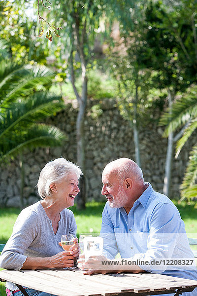 Älteres Ehepaar sitzt im Garten und genießt ein Glas Wein
