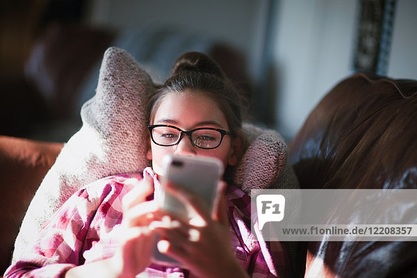 Mädchen entspannt sich auf dem Sofa und schaut auf ein Smartphone