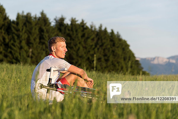 Junger männlicher Radfahrer sitzt im Feld und schaut hinaus