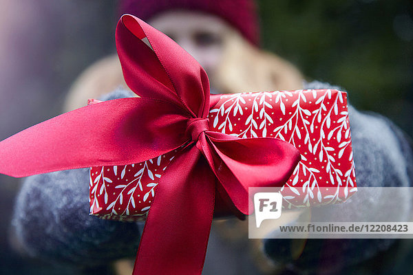 Frau hält Weihnachtsgeschenk mit roter Schleife hoch