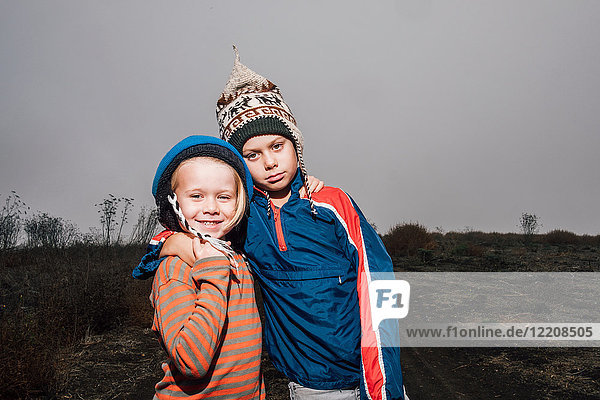 Portrait of two brothers outdoors wearing knitted hats arms around each other