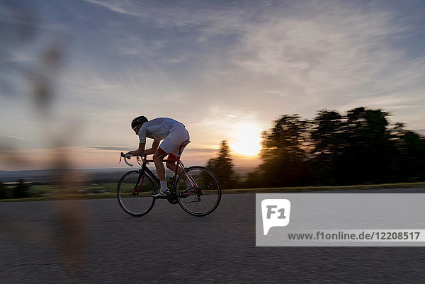 Young male cyclist cycling down rural road at sunset