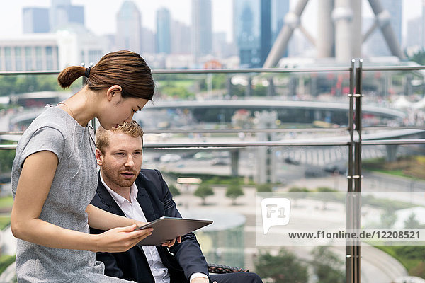 Junge Geschäftsfrau und Mann betrachten digitales Tablet im Bürgersteig-Café im Finanzzentrum von Shanghai  Shanghai  China