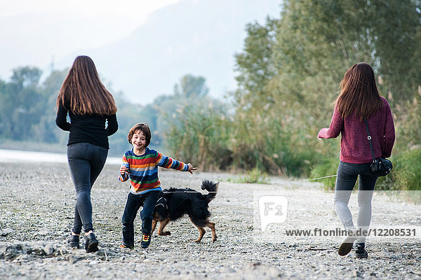 Junge mit jungen Frauen rennen mit Hund am Flussufer entlang  Calolziocorte  Lombardei  Italien