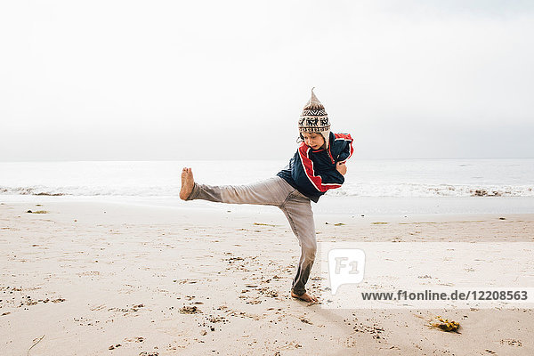 Young boy standing on beach balancing on one leg