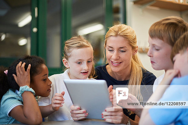 Lehrer mit Schülerinnen und Schülern  die sich im Klassenzimmer der Grundschule ein digitales Tablet ansehen
