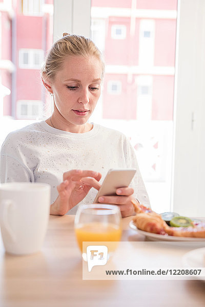 Junge Frau mit Smartphone-Touchscreen am Frühstückstisch