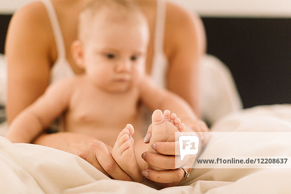 Woman holding baby daughters bare feet on bed  close up