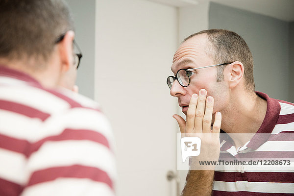 Over shoulder view of mature man looking at his face in bathroom mirror