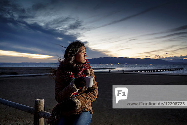 Young woman wrapped in scarf looking over her shoulder from beach at dusk  Tarragona  Catalonia  Spain