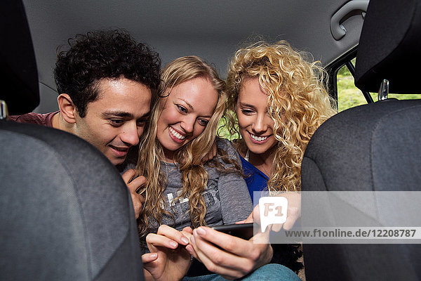Friends in back seat of car looking at smartphone