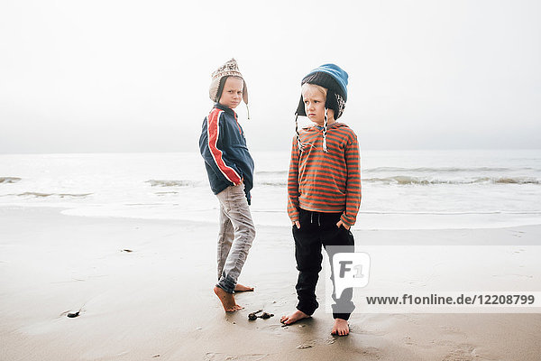 Portrait of two brothers standing on beach wearing knitted hats