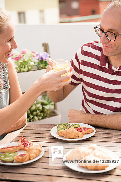 Junge Frau überreicht ihrem Freund am Terrassentisch Frühstücks-Orangensaft