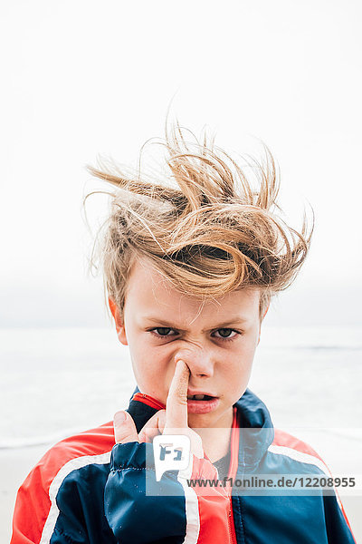 Portrait of boy on beach messy hair poking finger up nose close-up