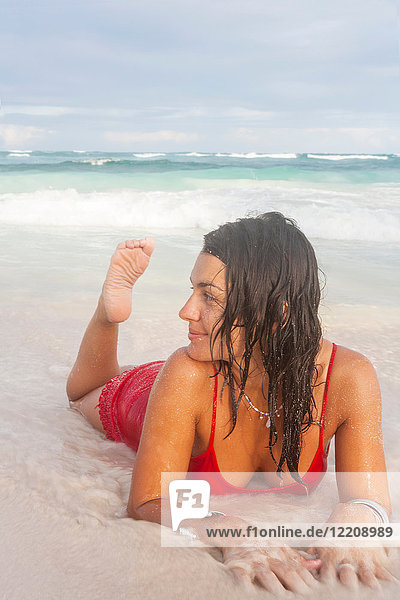 Young woman in red swimming costume lying on beach at water's edge  Tulum  Quintana Roo  Mexico